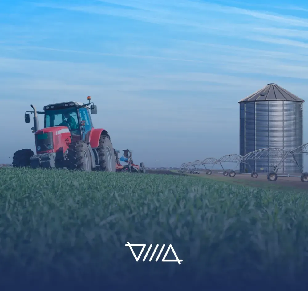 Tractor rojo en un cultivo verde junto a un silo, imagen del sector agroindustrial