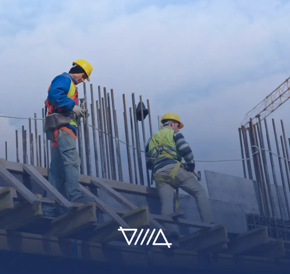 Dos obreros con casco y arnés trabajan sobre el encofrado de una obra en construcción