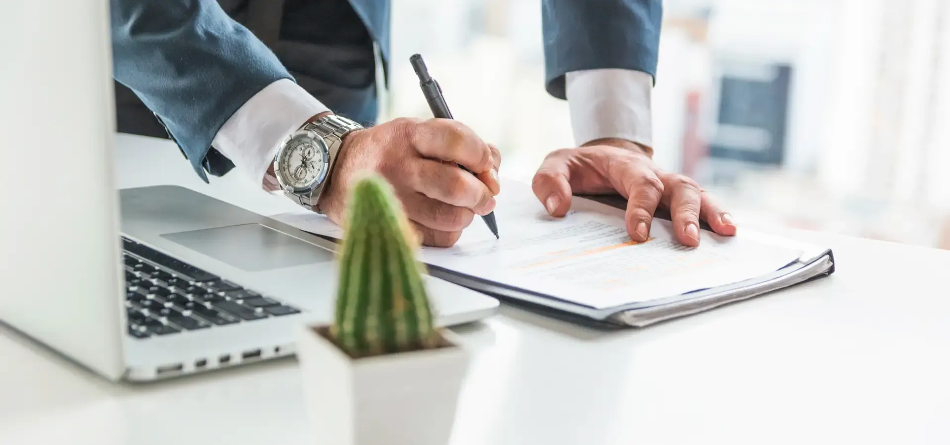 Manos firmando un contrato junto a una laptop y un cactus, Legal Card 365