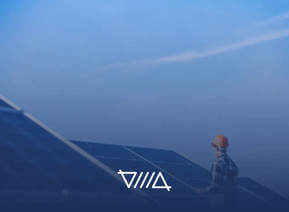 Trabajador con casco naranja junto a paneles solares bajo un cielo azul, transición energética